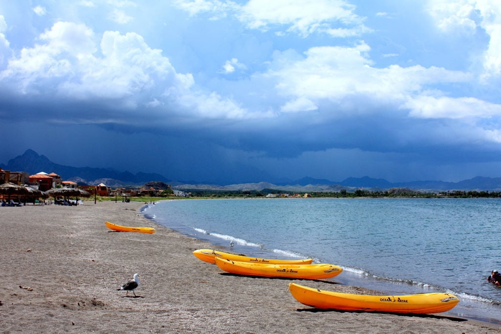 Bright orange kayaks on a sandy beach in Loreto. In this Loreto travel guide, Day 4 includes kayaking around snorkeling spots in Loreto, Mexico.