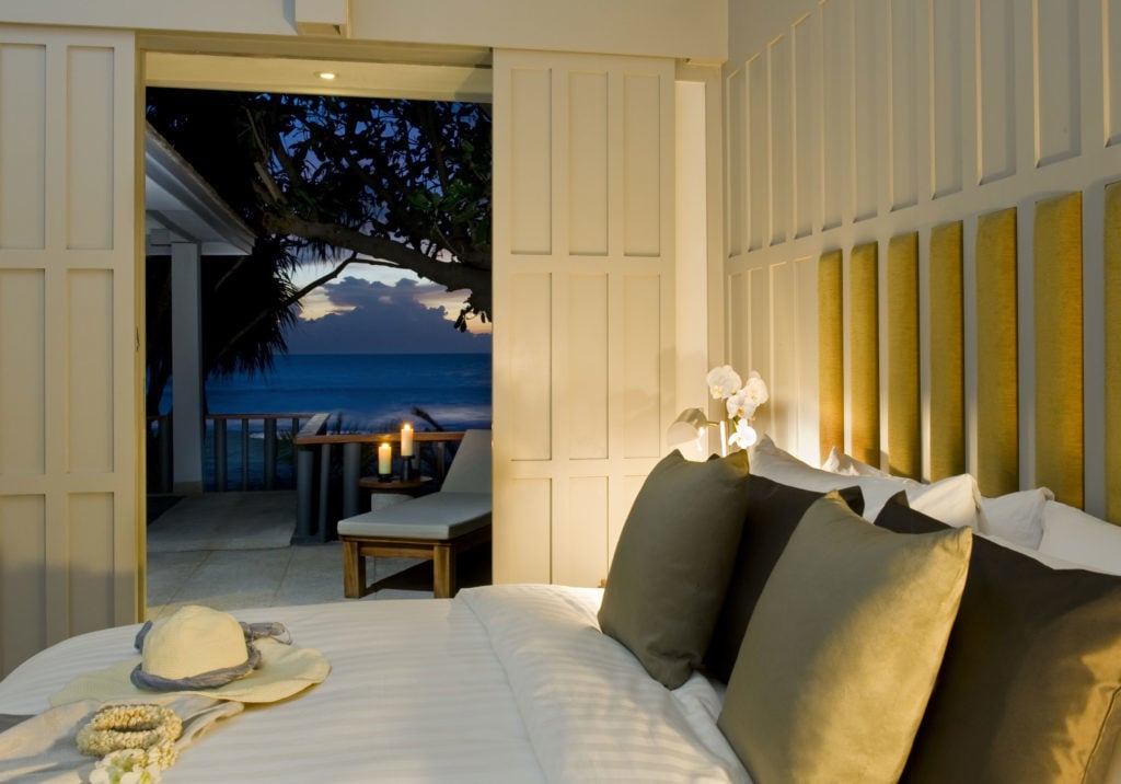 Comfy bed with the view of the beach outside at night. The Surin Phuket is one of the affordable 5-star resorts in Phuket.