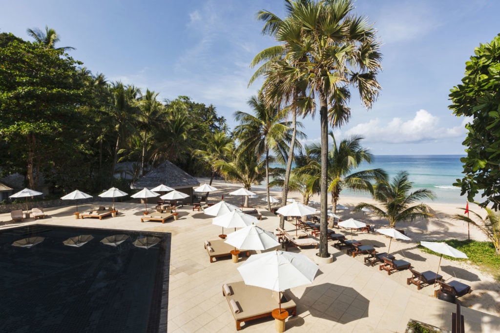 Swimming pool surrounded with comfy lounge chairs by the beach