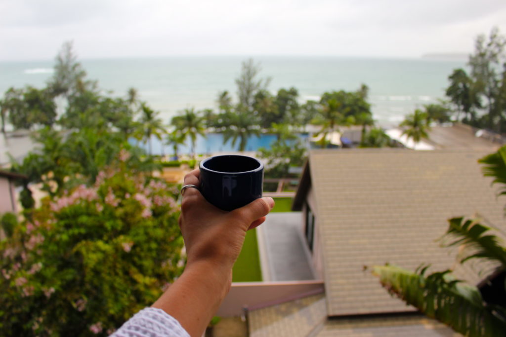 Holding up a cup of coffee while overlooking the infinity pool from the room of Hyatt Regency Phuket