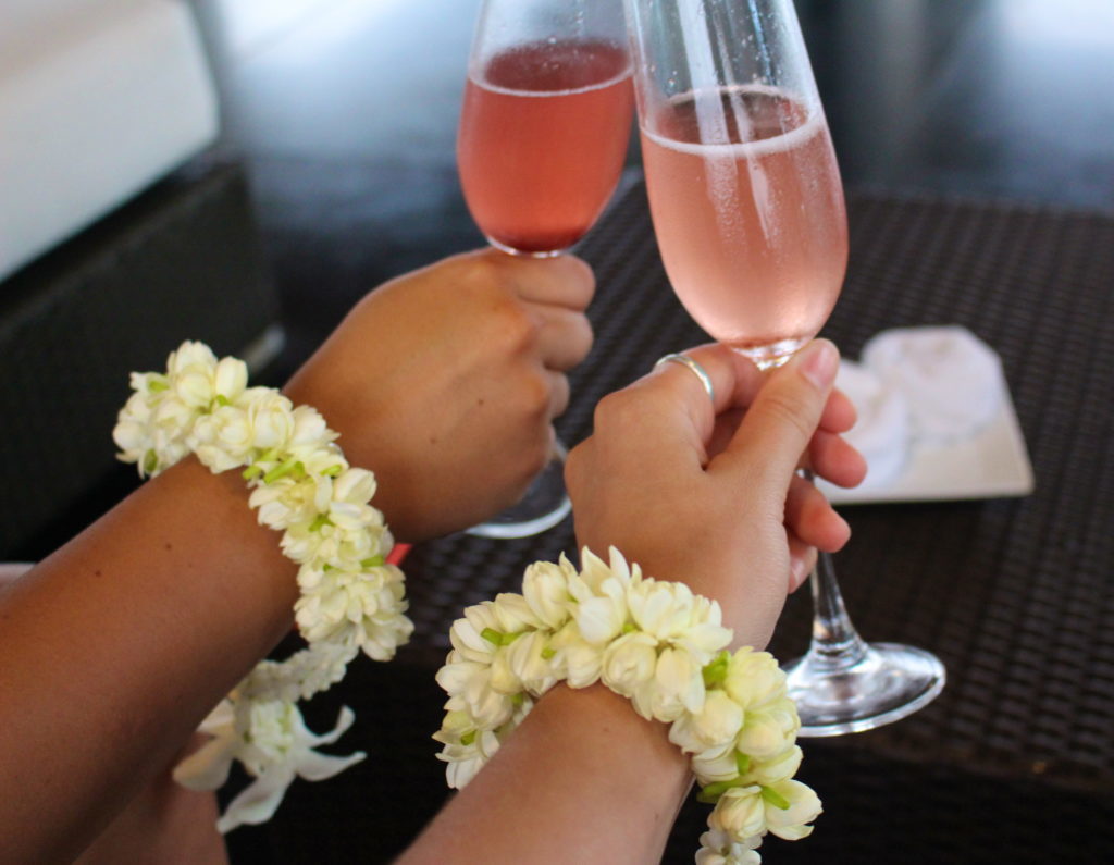Holding two glasses of champagne with flower garlands on our wrists