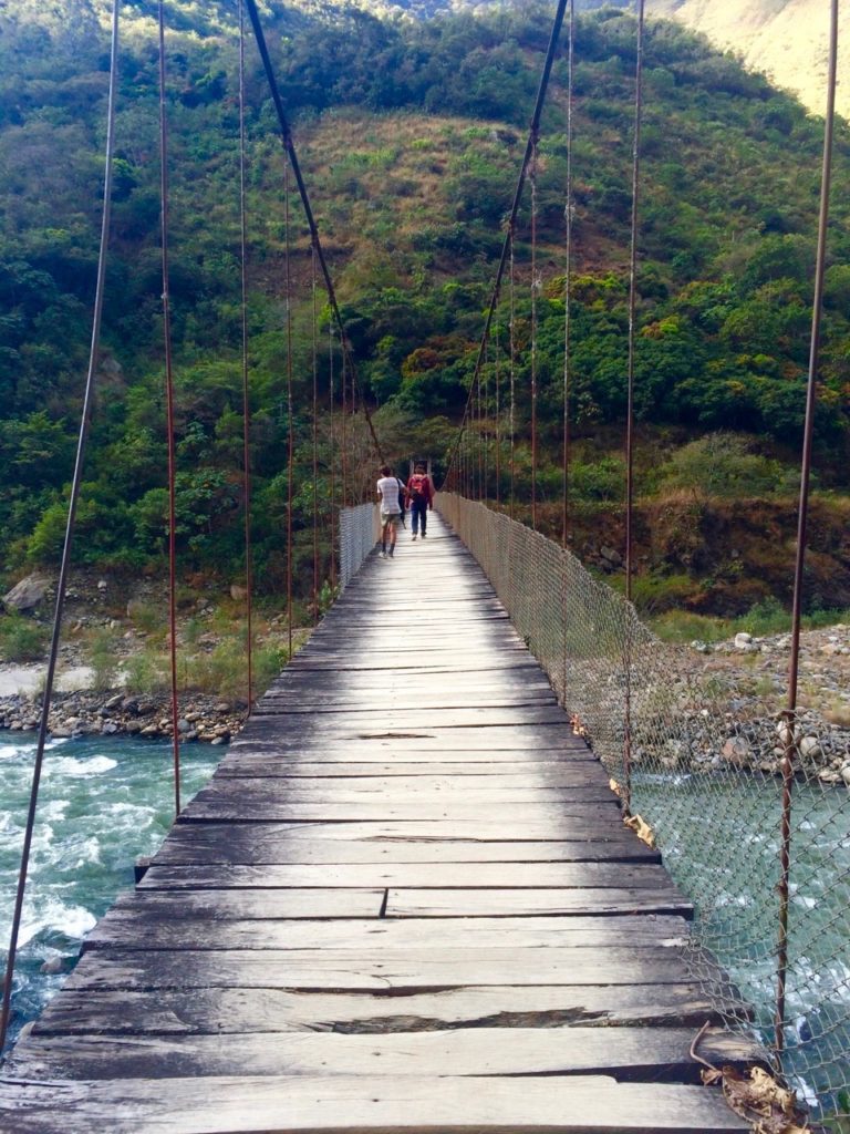 An old wooden bridge over the river where people can pass during the Inca Jungle Trek