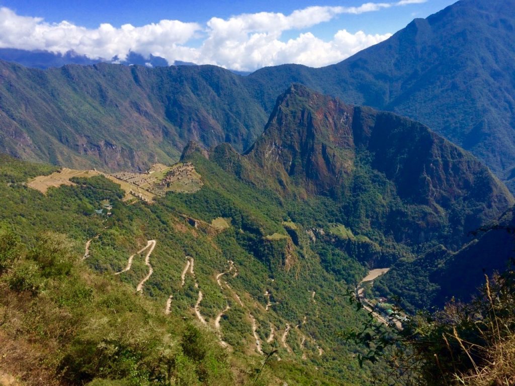 View of the Machu Picchu from afar surrounded by lush forests and higher mountain peaks