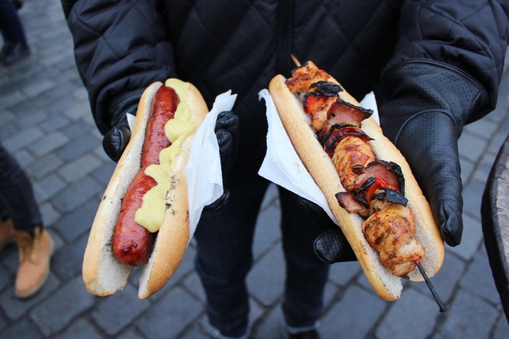 Holding Czech paprika sausages with mustard, and chicken skewers with Prague ham, peppers, and sweet onions