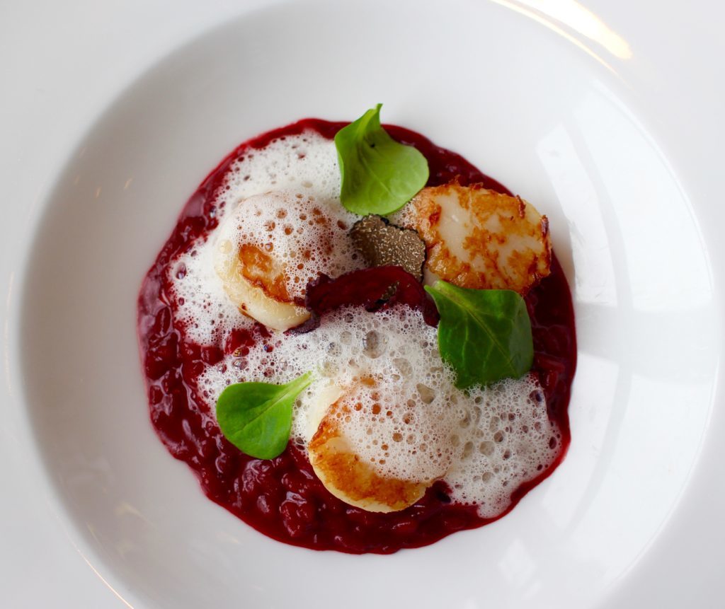 Dish of seared scallops, atop a beetroot risotto, with beetroot chips, and a generous shaving of black truffle