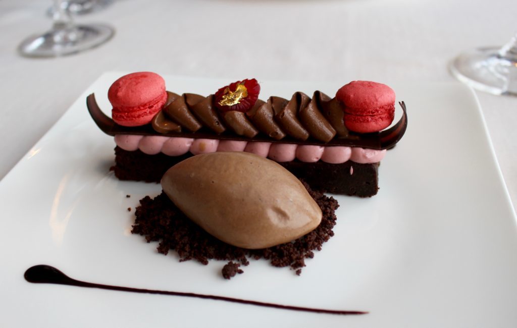 Cold chocolate fondant complete with a light raspberry foam, fluffy raspberry macarons, chocolate ice cream, and luxurious gold shavings - the dessert in our fine dining in Prague