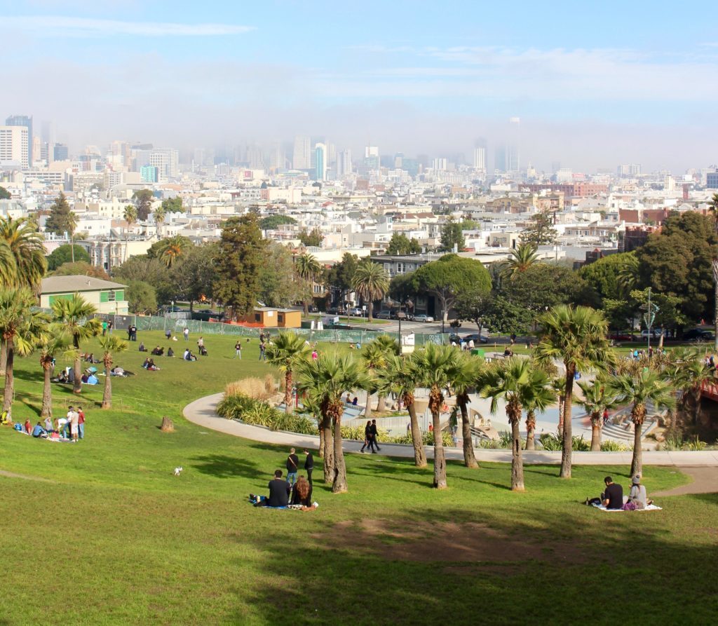 People relaxing in Dolores Park on a sunny day. Setting up a picnic at Mission Dolores Park is one of the underrated things to do in San Francisco.