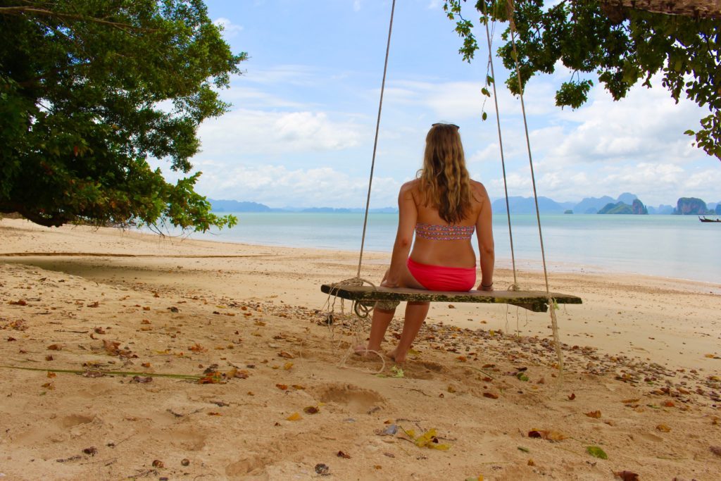 Maddy sitting on a wooden swing on the sandy beach