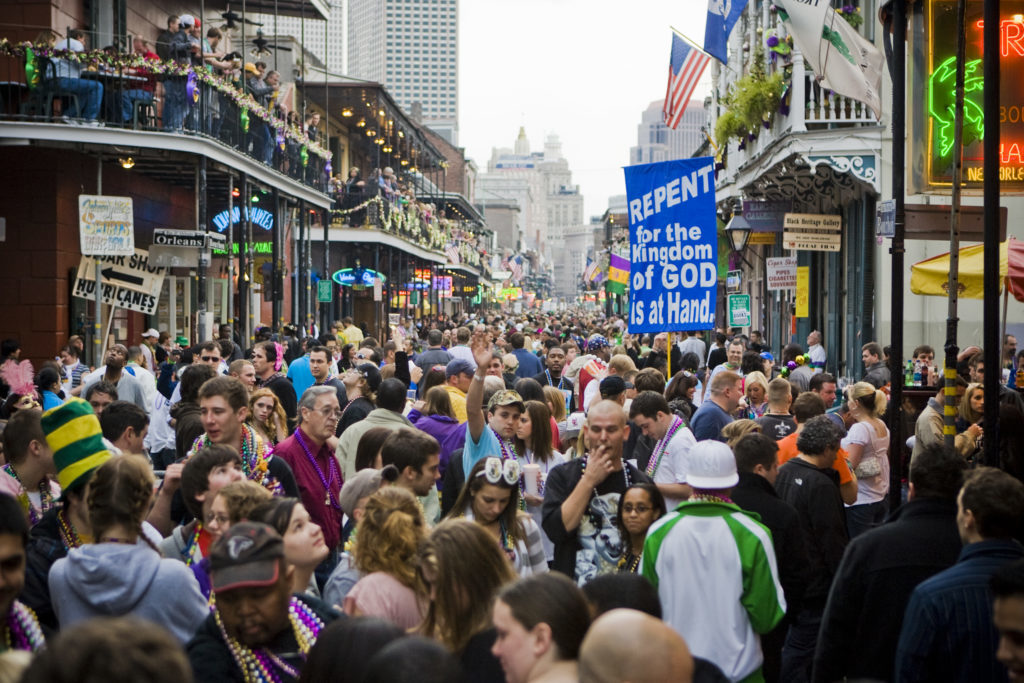 People crowding a street in New Orleans in celebration of Mardi Gras. The Mardi Gras in NOLA is one of the 20 festivals to experience in your 20s.