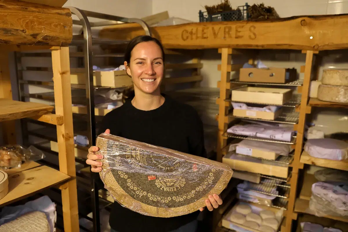 Maddy holding a large wheel of cheese inside a cheesemonger's cellar in Paris.