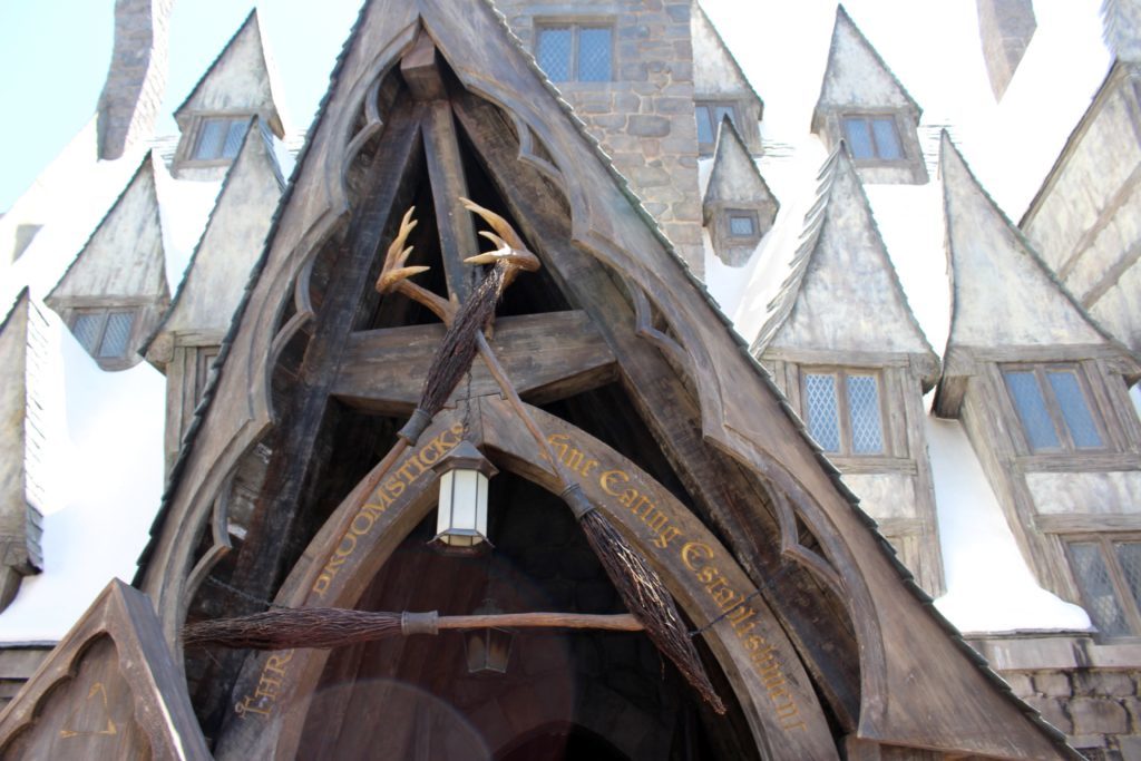 Three broomsticks displayed triangularly in front of a sign "THREE BROOMSTICKS - FINE EATING ESTABLISHMENT"