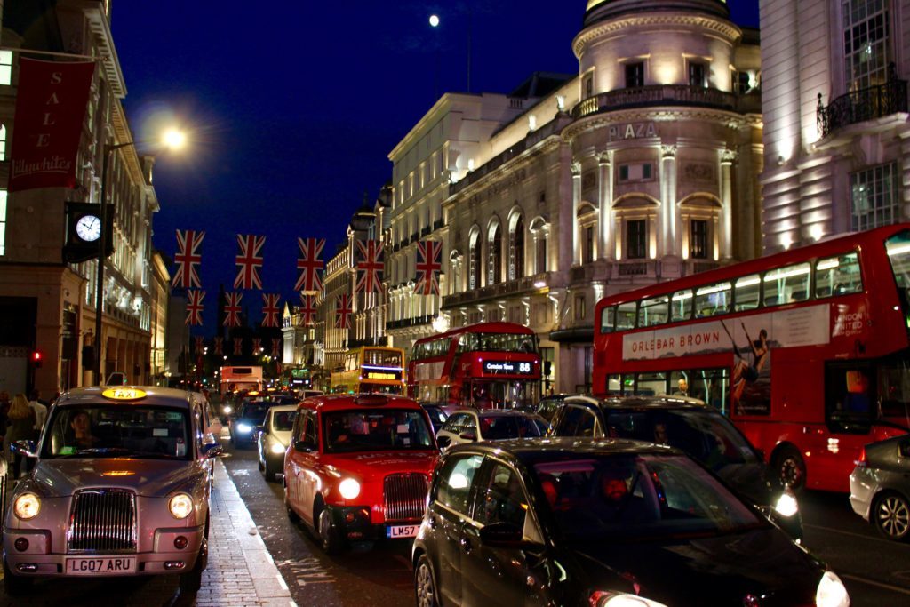 Busy London street at night showing taxi cabs and red double decker buses