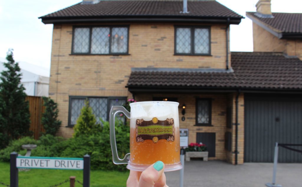 Holding up a cup of Butterbeer outside Harry Potter's home at Privet Drive