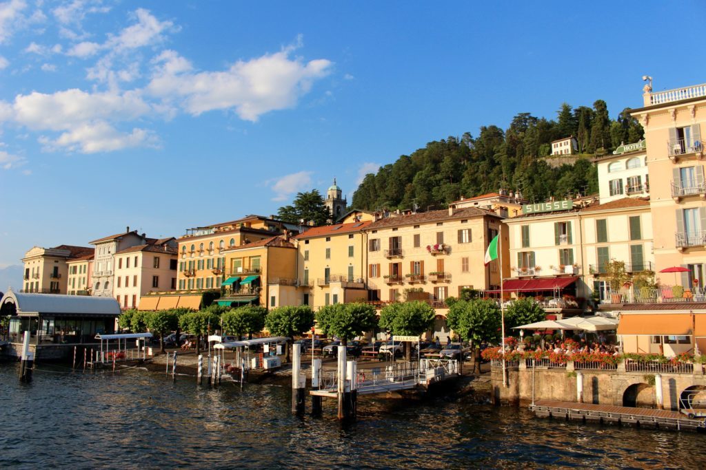 Bellagio pier in front of tall buildings facing the sun. In this Lake Como travel guide, you'll find the best things to do in Bellagio.