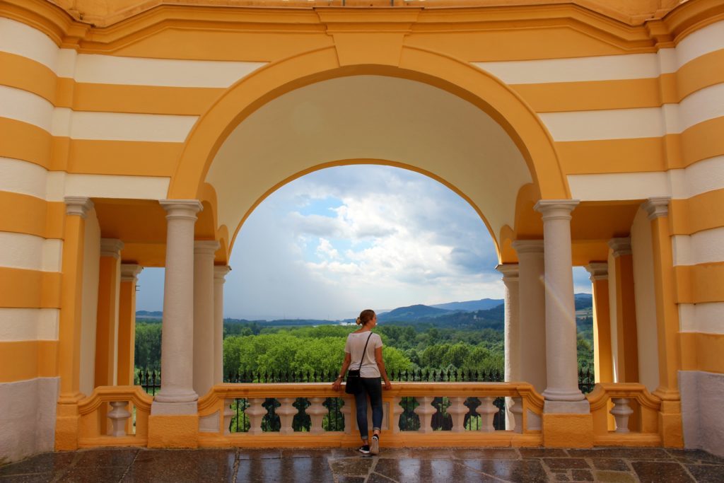 Maddy, blogger, on an arched balcony at the Melk Abbey, overlooking a beautiful forest and mountain views. Discover the treasures of Austria when you book your Viking River Cruises Grand European Tour.