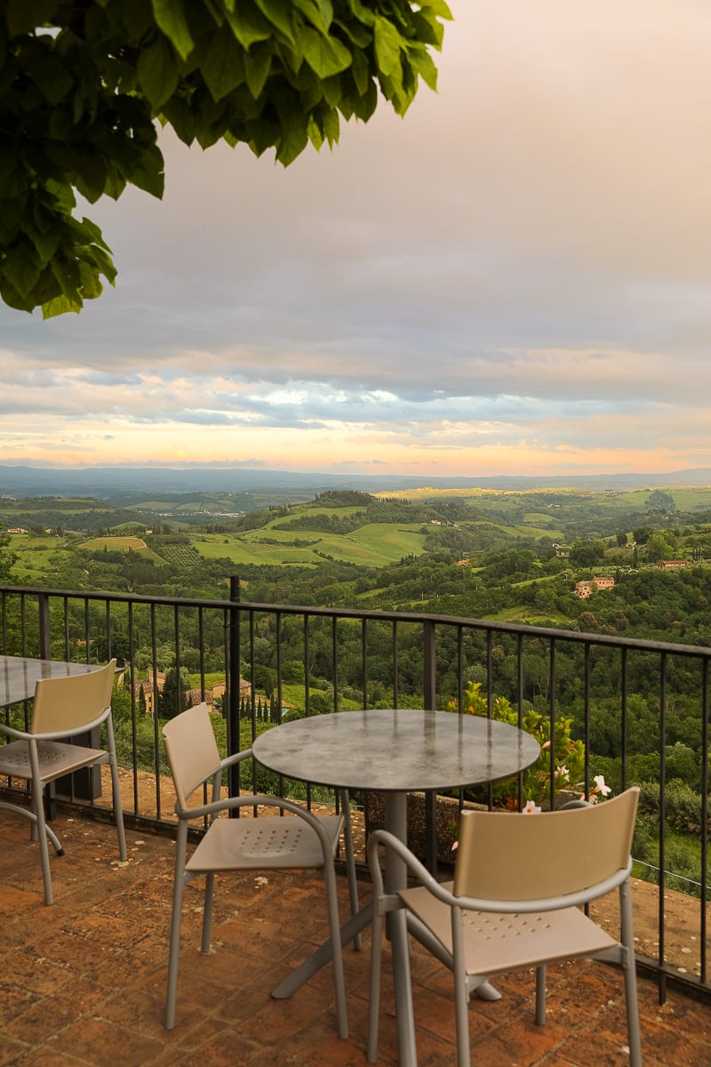 Dining area on a terrace overlooking the green hills of San Gimignano. Make sure to visit this town in Tuscany in one day.