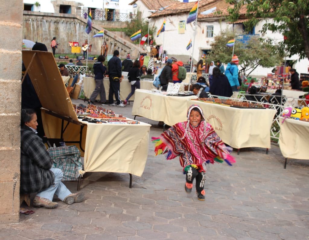Kid in traditional clothing happily running around the souvenir stalls in Plaza San Blas
