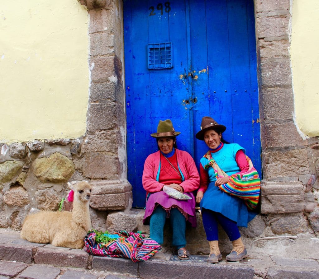 Two local Cusco women in traditional clothes and an alpaca sitting on a doorstep. Expect to see similar sights during your three days in Cusco.