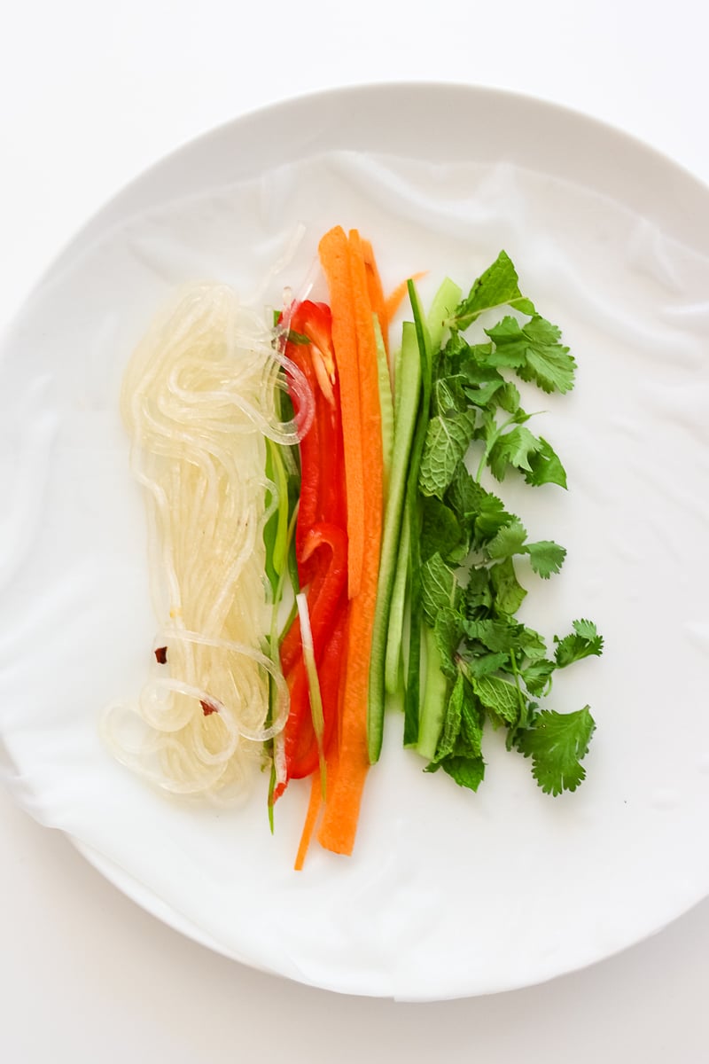 Vegetables and noodles on top of a piece of rice paper, before rolling it into a spring roll.