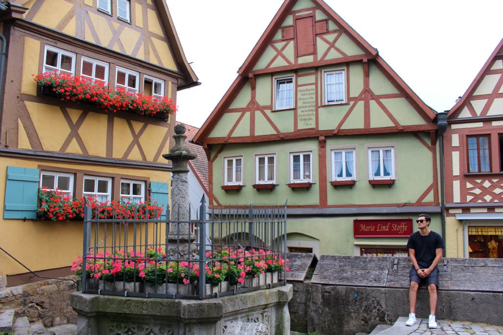 Mauricio, blogger, sitting on a stone fence surrounded by the old buildings of Rothenburg ob der Tauber