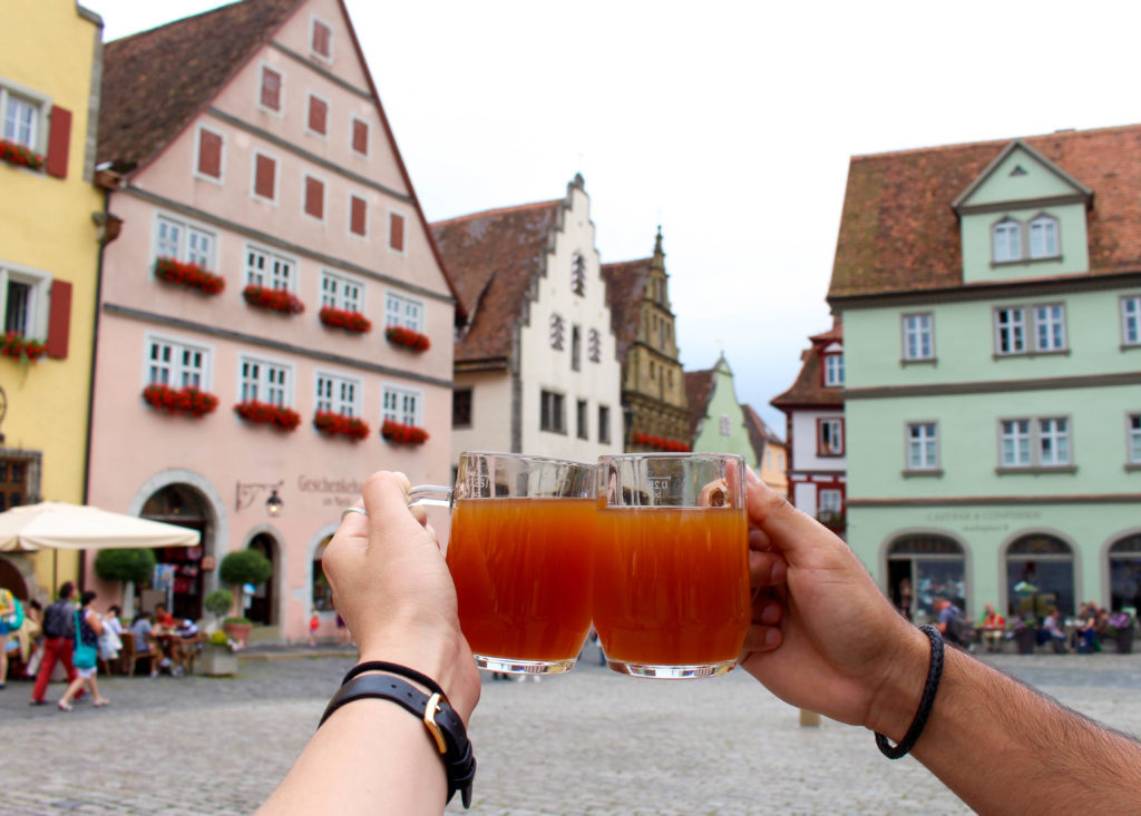 Holding up two mugs of drinks with the city's medieval buildings as the background