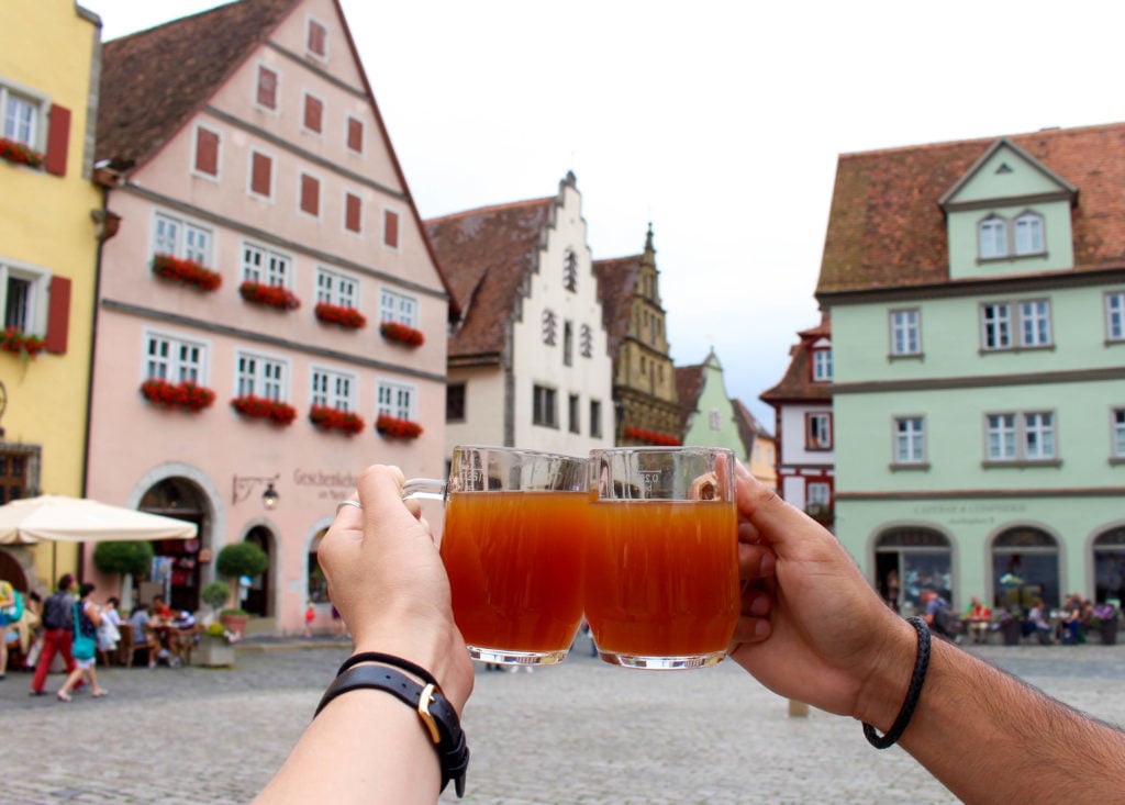 Holding up two mugs of drinks with the city's medieval buildings as the background