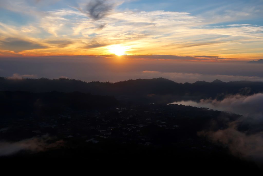 Sun slowly rising up behind the clouds and silhouettes of mountains