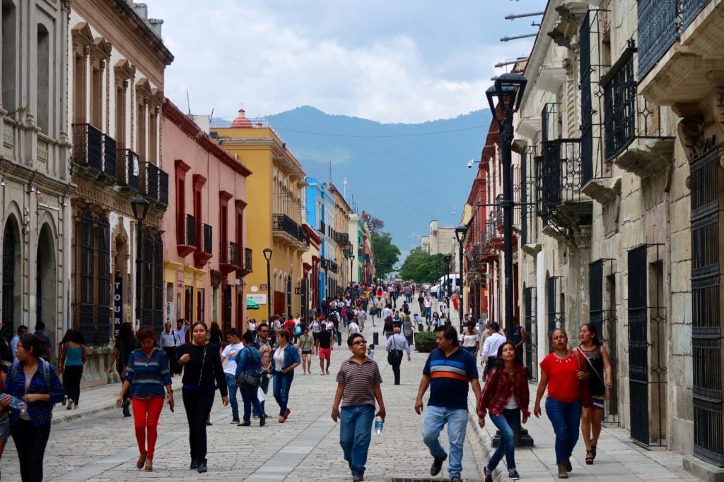 Crowd of people roaming around a colorful street in Mexico. If you're wondering where to stay in Oaxaca City, this guide contains a list of recommended hotels to stay in.