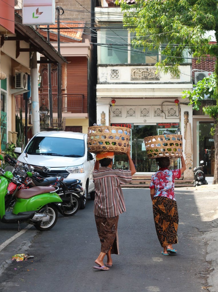 Two local vendors holding up baskets on their head while selling along the road