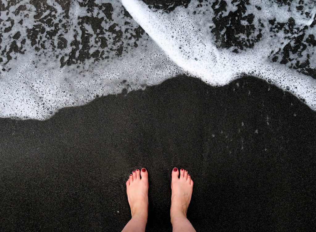 Feet on black sand beach in Pemuteran 