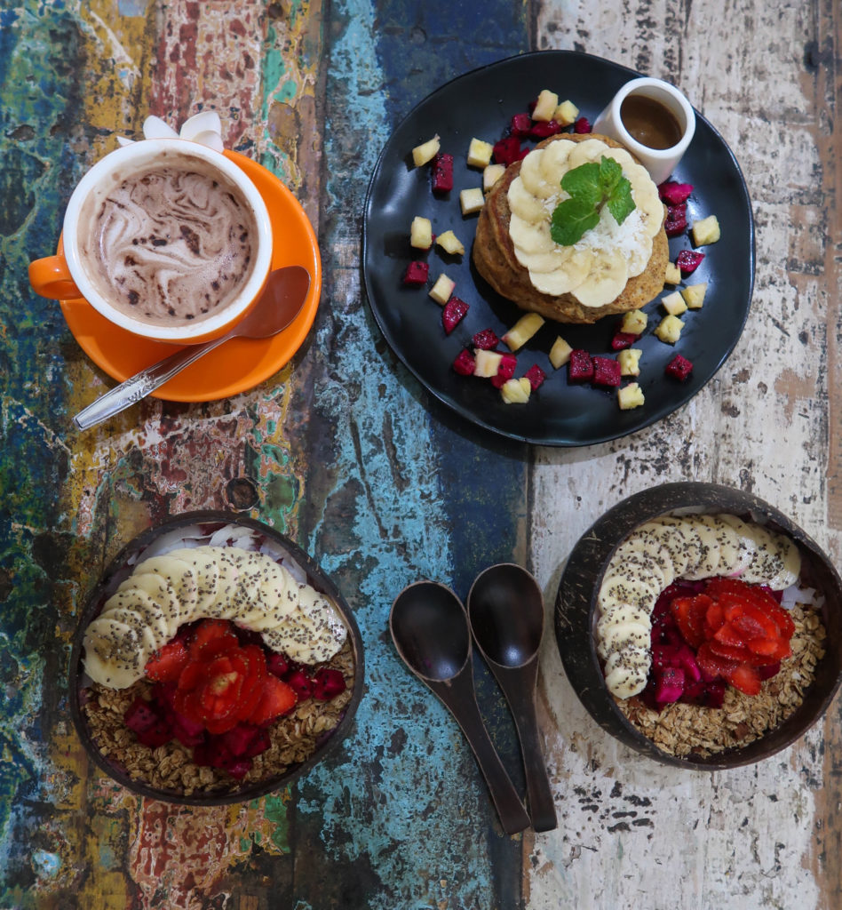 Delicious acai bowls and a cup of coffee on a wooden table. Try out the many food spots in Seminyak during your three weeks in Bali.