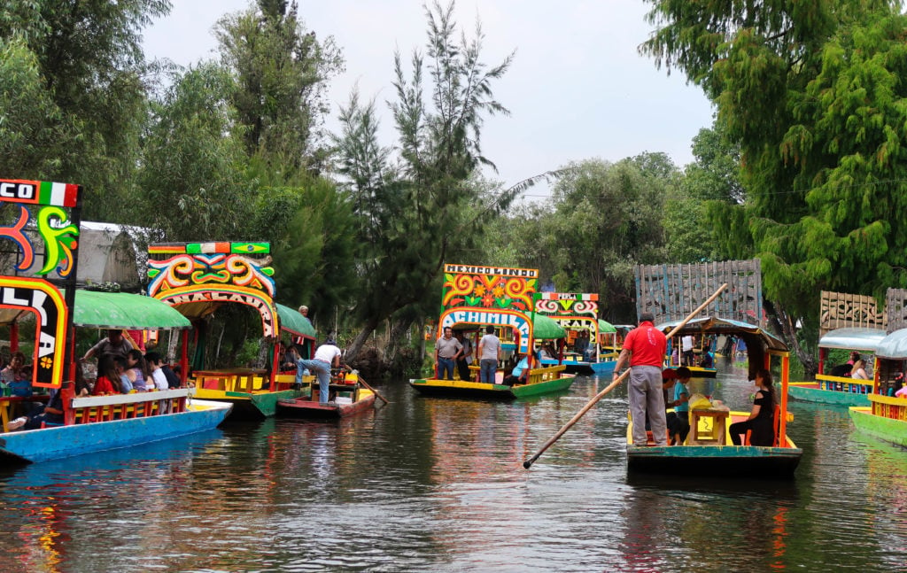 Colorful, decorated boats sailing on a canal. In this Mexico City foodie guide, we highly recommend experiencing dining on a boat while enjoying your food.