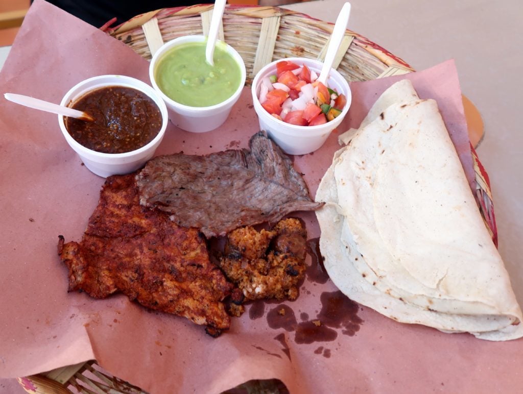 A plate of enfrijolada, with cups of different sauces, spices, and grilled meat