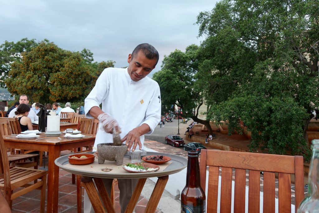 A chef using mortar and pestle while preparing food on an outdoor restaurant table