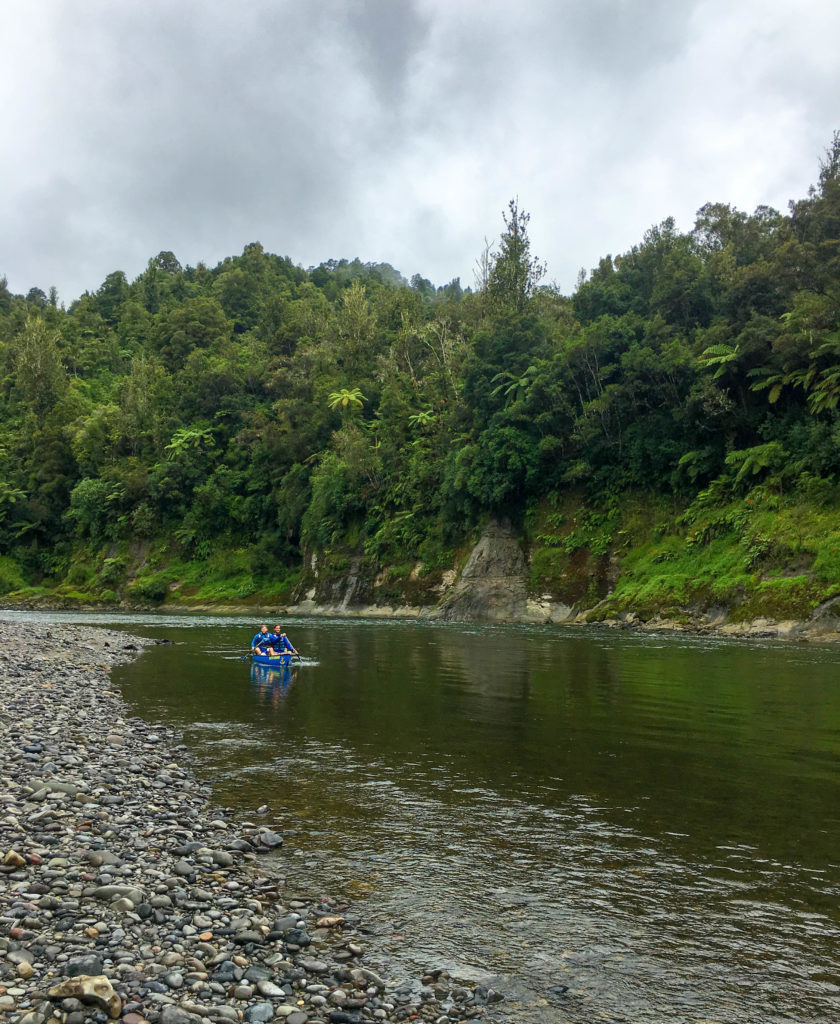 Rowing a canoe on the calm river surrounded by lush forest trees under cloudy skies. On the second day of our Whanganui River Journey, we did a hike and situated on a sacred land.