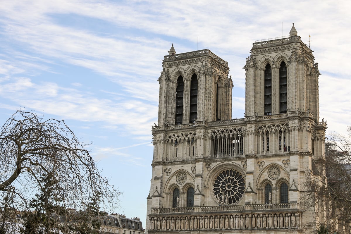 The facade of the Notre Dame in Paris on a partly cloudy day surrounded by leafless trees in the winter