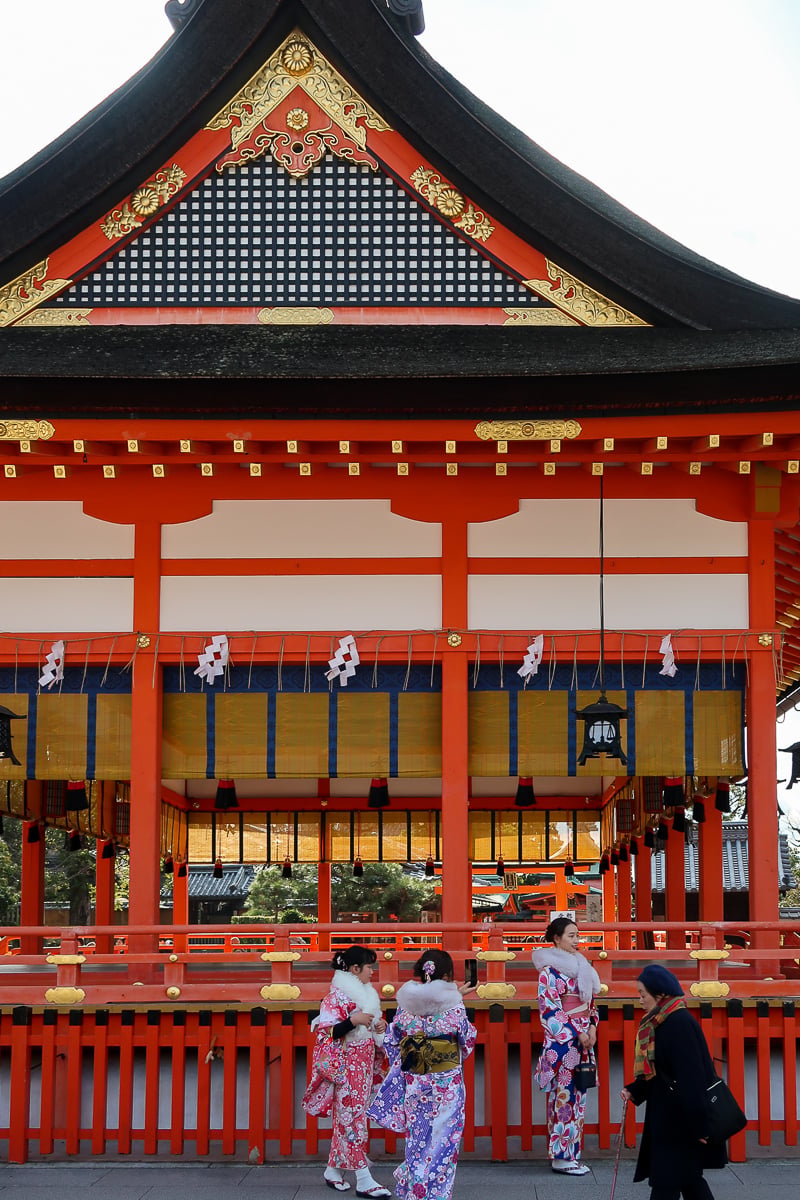 Women in colorful kimono outside a vermilion shrine building at Fushimi Inari Taisha in Kyoto