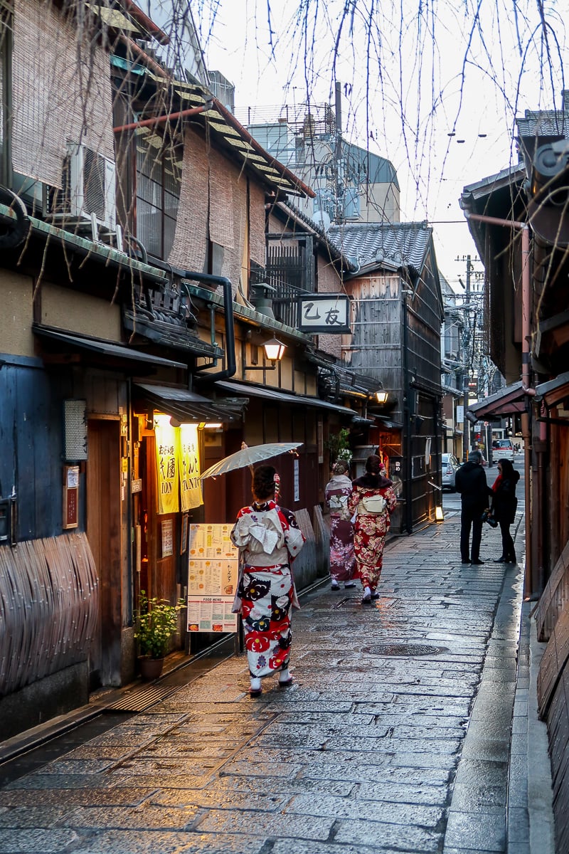 Women in kimono walking along a narrow traditional street lined with wooden buildings in Gion, Kyoto