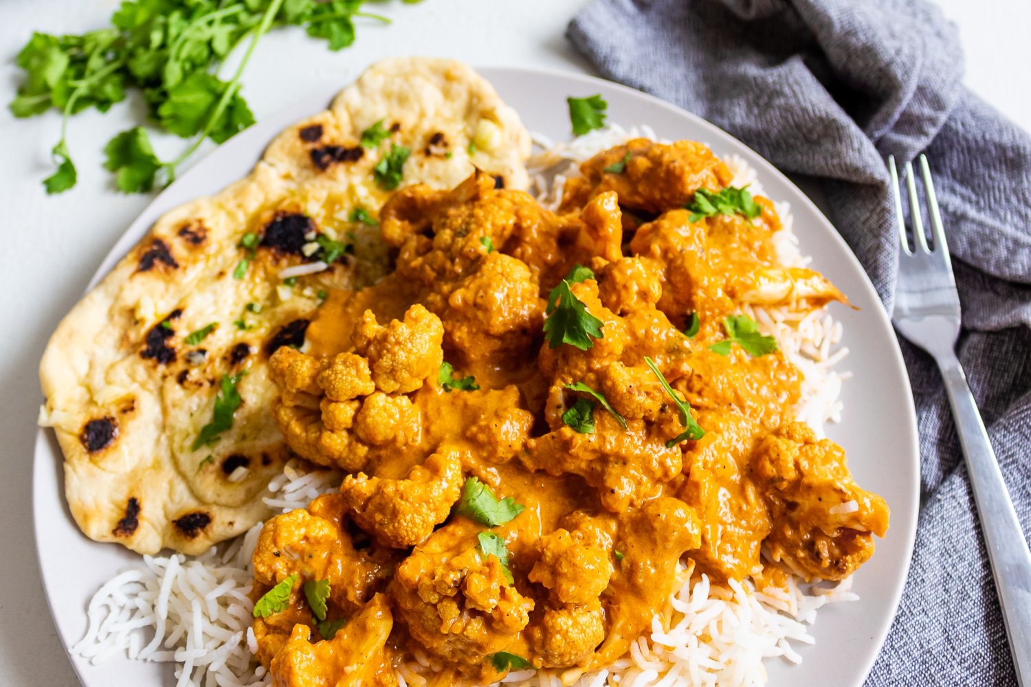 A plate of delicious cauliflower tikka masala on a bed of white rice with garlic naan bread on the side