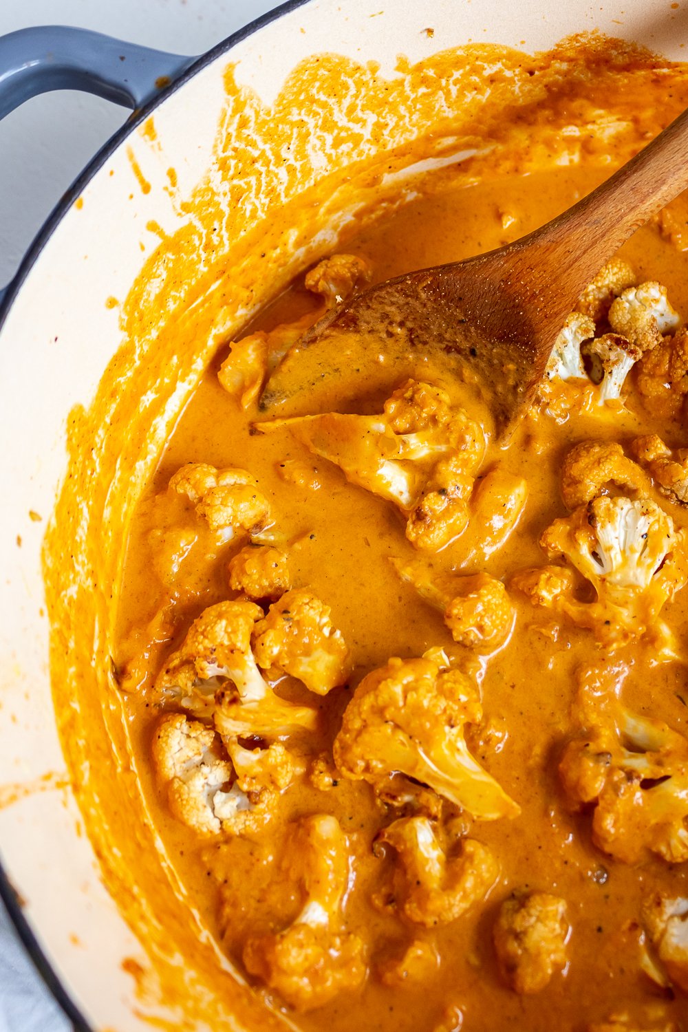 stirring roasted cauliflower into a pot of creamy orange-colored tikka masala sauce