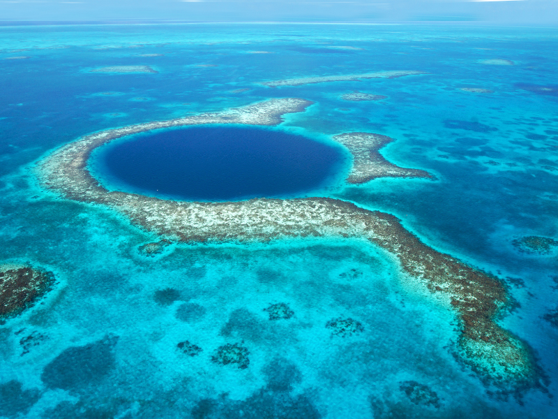 Aerial view of the Belize Barrier Reef Reserve System showing its magnificent form and blue waters. If you're wondering if and why you should travel to Belize for your next vacation, the amazing snorkeling and diving, and the opportunity to visit the Blue Hole is on top of my list.