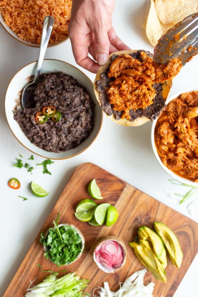 Assembling vegan tostadas with refried black beans, cabbage, onion, cilantro, avocado, and more.