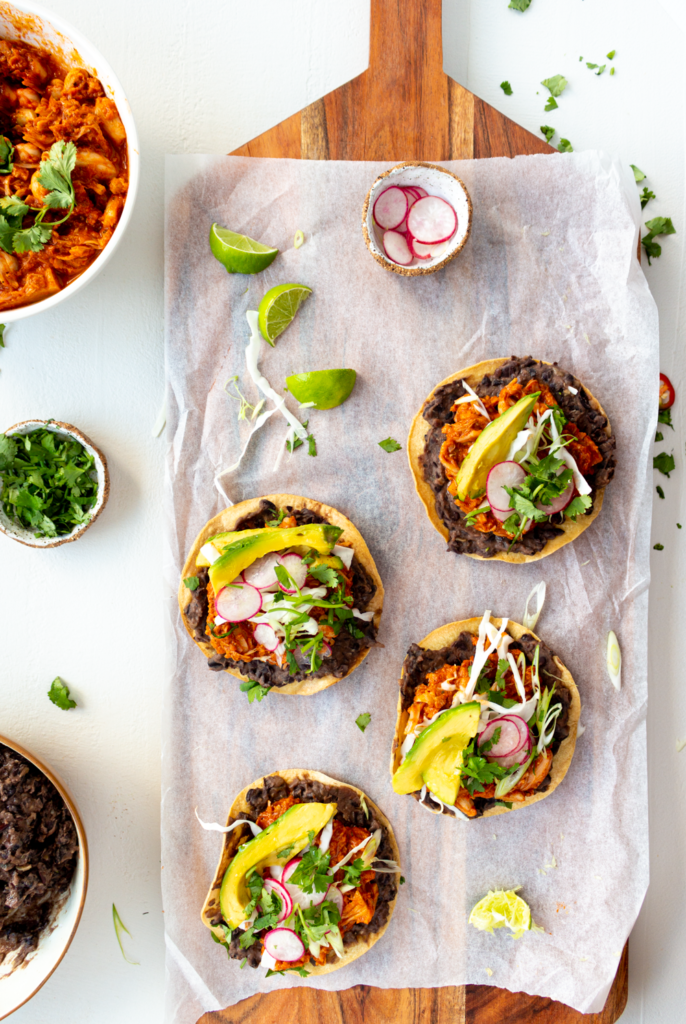 Jackfruit Tinga Tostadas make for an easy and delicious Mexican-inspired dinner! These tostadas are crispy, slathered with flavor-packed refried black beans, then topped with smoky, meaty pulled jackfruit. Quick, healthy, and flavor-packed, you'll love this Vegan Jackfruit Tinga in tostadas, tacos, and burritos!