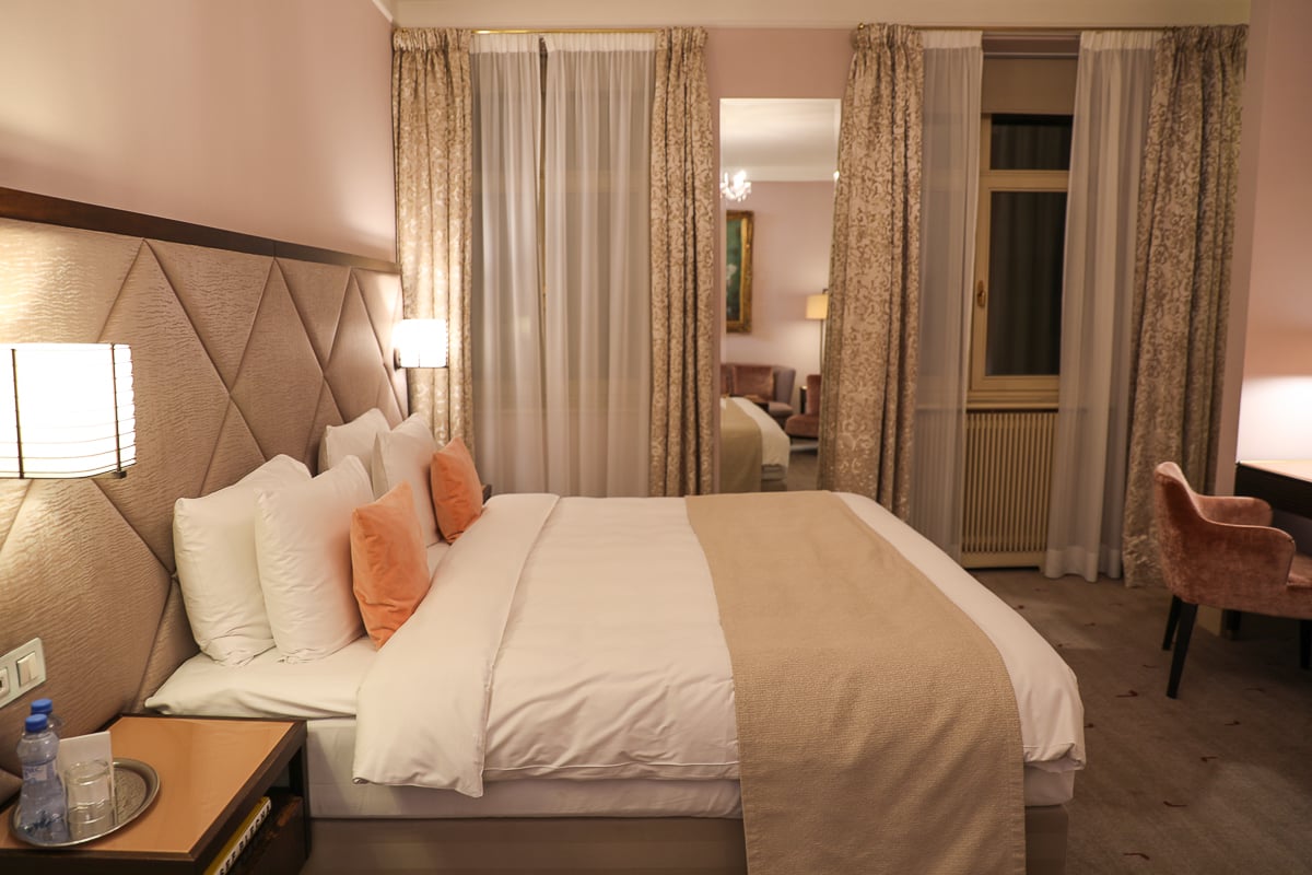 Elegant guest room at Aria Hotel Prague with plush king bed, peach accent pillows, soft lighting, and classic draped curtains.