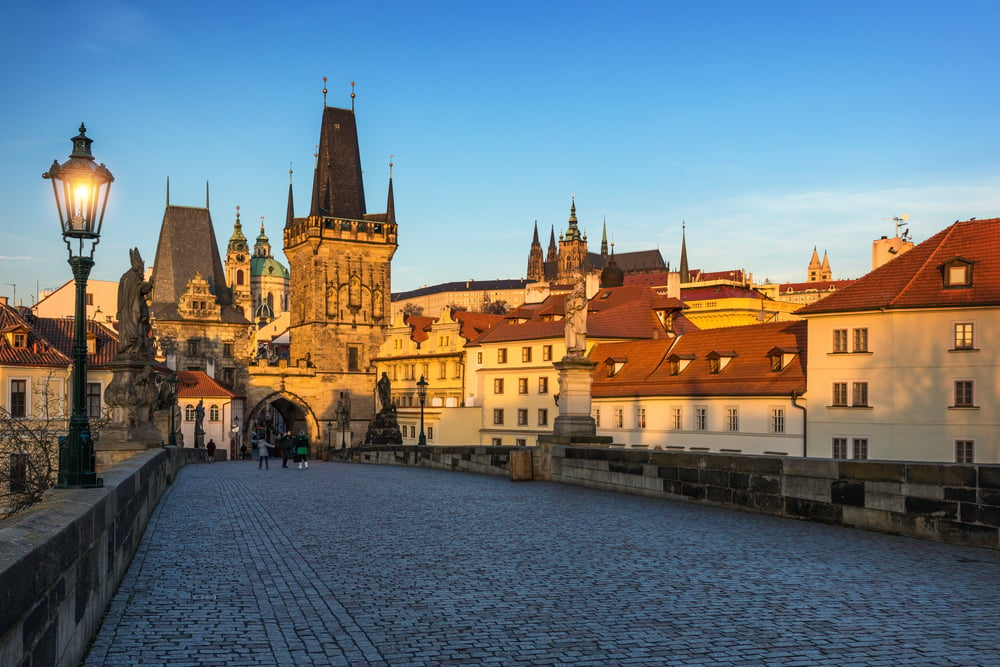 People walking across Charles Bridge as the sun starts to rise