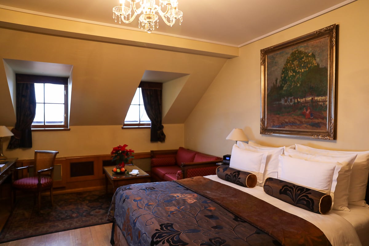 Charming guest room at the Golden Well Hotel in Prague, with slanted windows, chandelier lighting, elegant furnishings, and a cozy seating area.