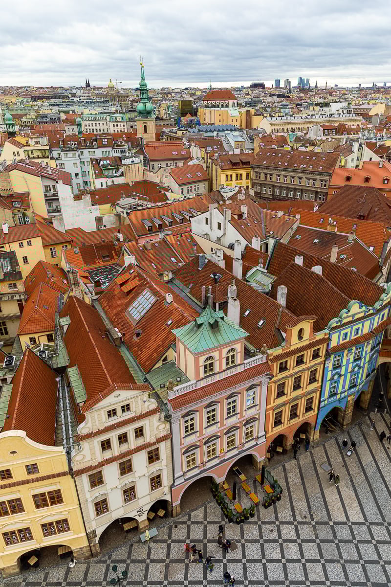 Aerial view over Old Town Square in Prague, showing colorful historic buildings, red rooftops, and cobblestone streets.
