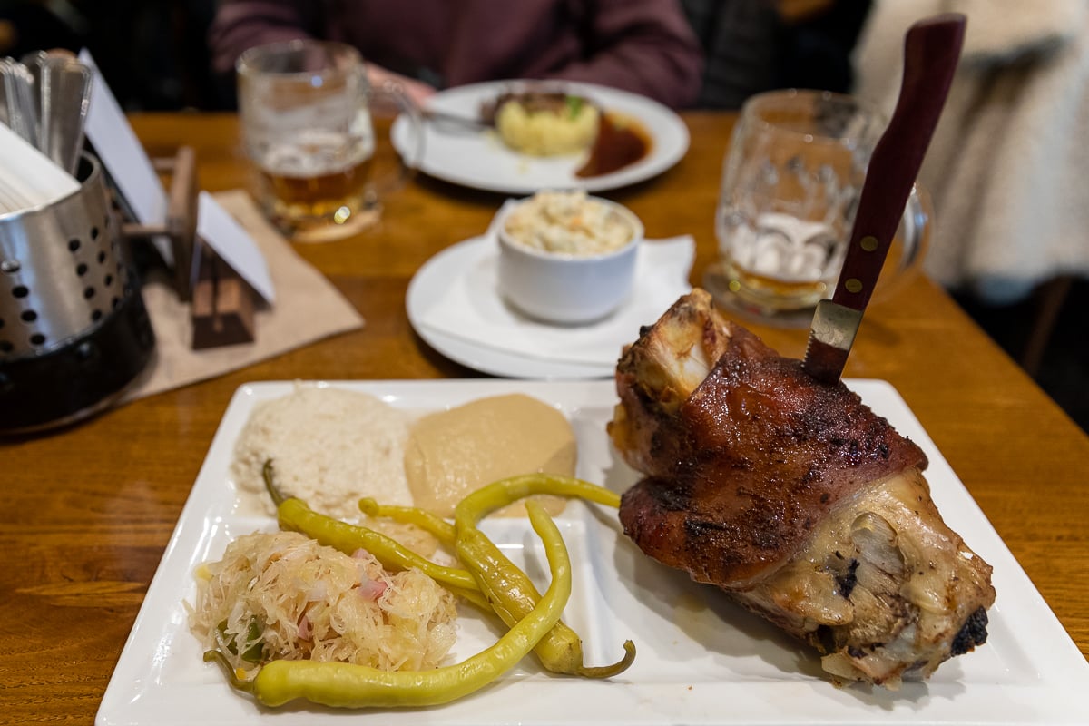 Traditional Czech roasted pork knee served with sauerkraut, horseradish, pickled peppers, and mustard at Bredovský Dvůr in Prague.