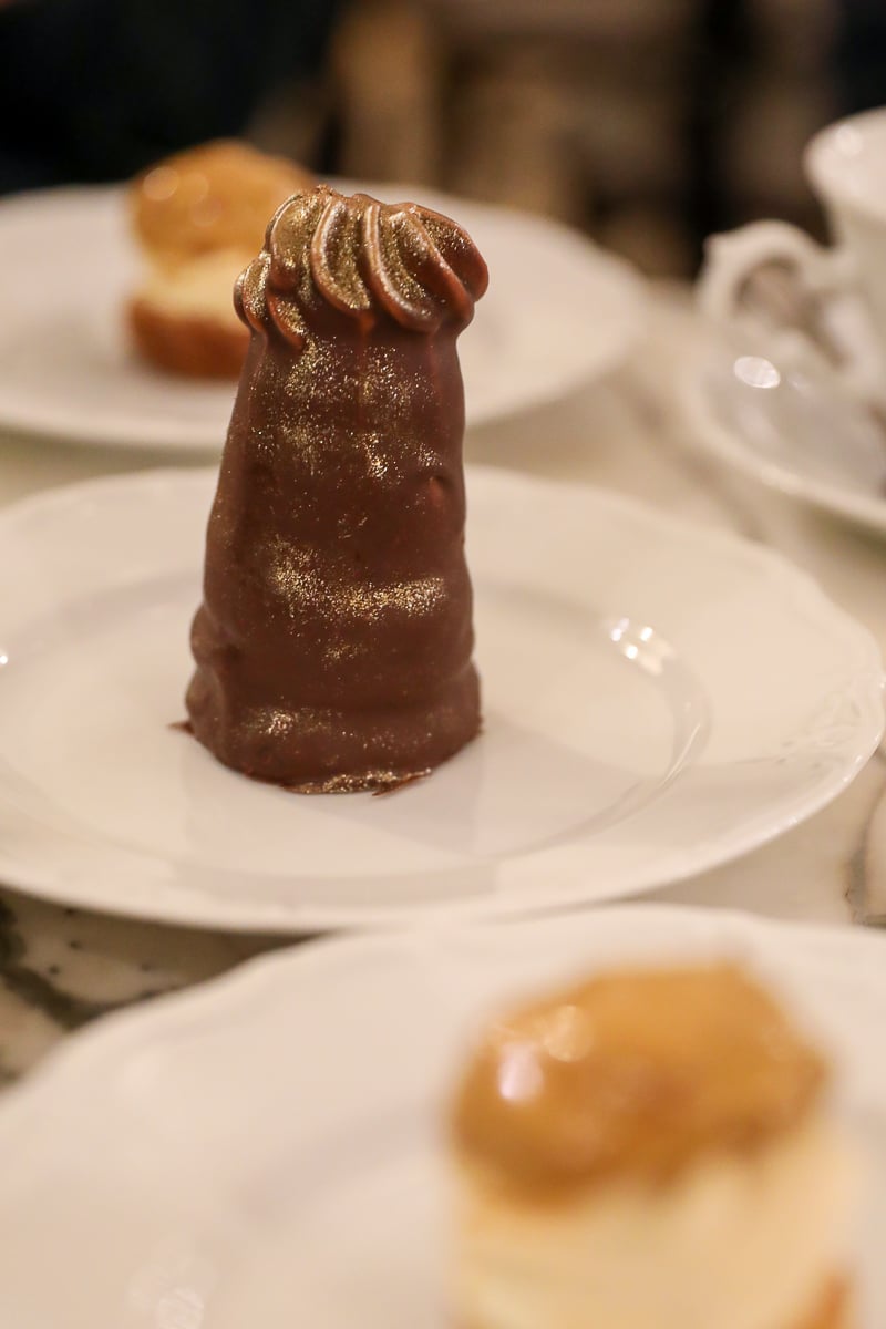 Traditional Czech dessert at a Prague café, featuring a tall chocolate-coated treat with a gold shimmer served on a white plate.