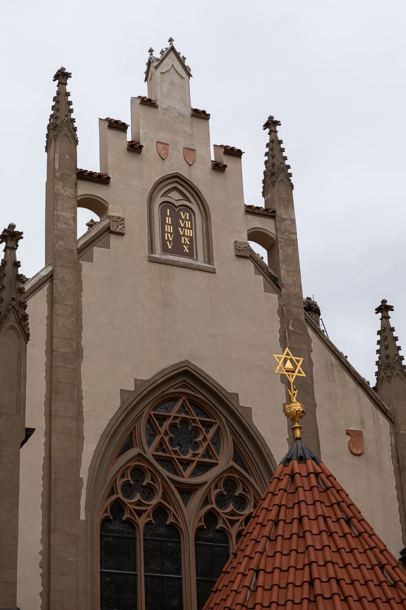 Exterior of the Old-New Synagogue in Prague’s Jewish Quarter, with Gothic spires, a Roman numeral clock, and golden Star of David detail.